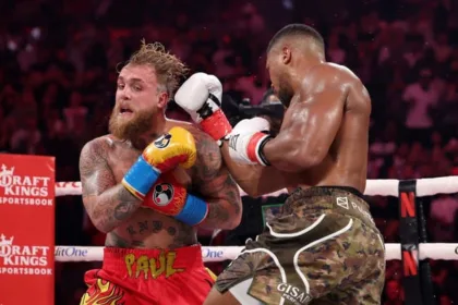 Anthony Joshua Landing A Powerful Punch On Jake Paul Inside A Boxing Ring With Spectators In The Background